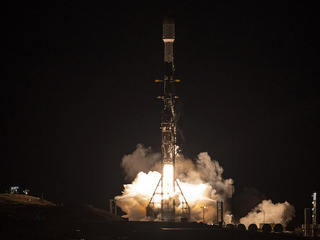 Photograph shows nighttime launch of SWOT satellite, just rising off its platform in an orange-white cloud of rocket exhaust.